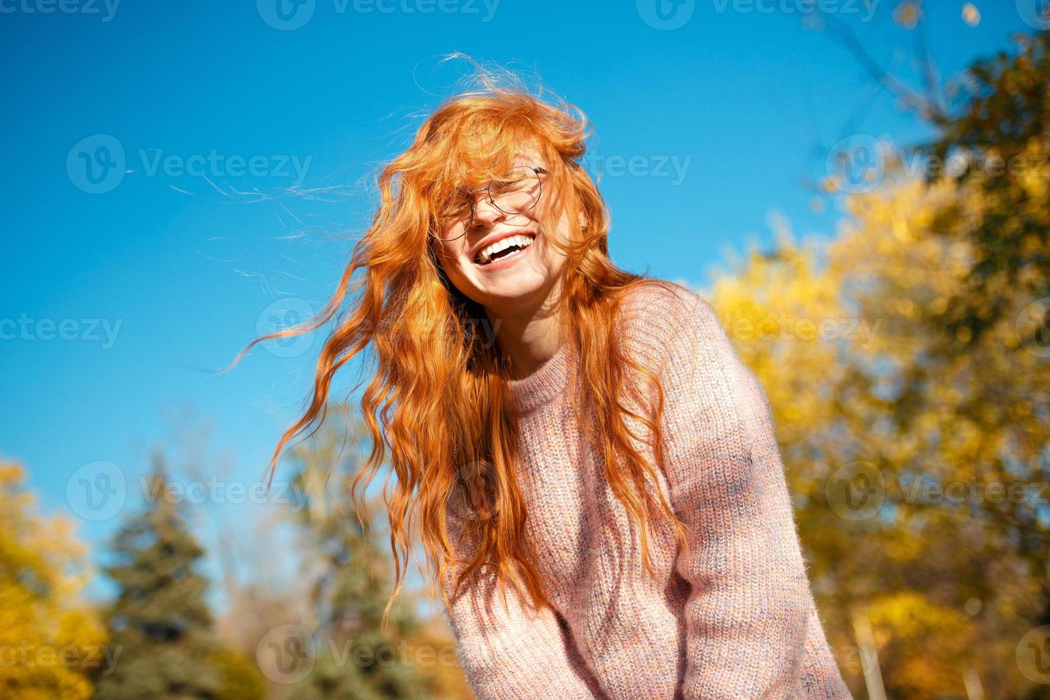 ritratti di un'affascinante ragazza dai capelli rossi con un viso carino. ragazza in posa nel parco autunnale con un maglione e una gonna color corallo. la ragazza ha un umore meraviglioso foto