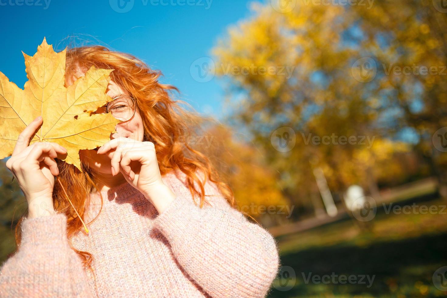 ritratti di un'affascinante ragazza dai capelli rossi con un viso carino. ragazza in posa nel parco autunnale con un maglione e una gonna color corallo. nelle mani di una ragazza una foglia gialla foto