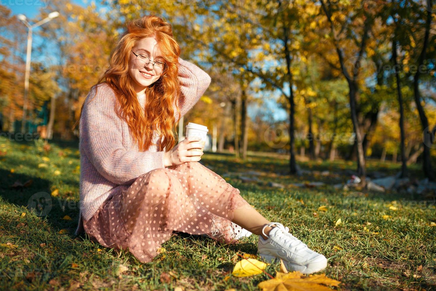 ritratti di un'affascinante ragazza dai capelli rossi con occhiali e un bel viso. ragazza in posa nel parco autunnale con un maglione e una gonna color corallo. foto
