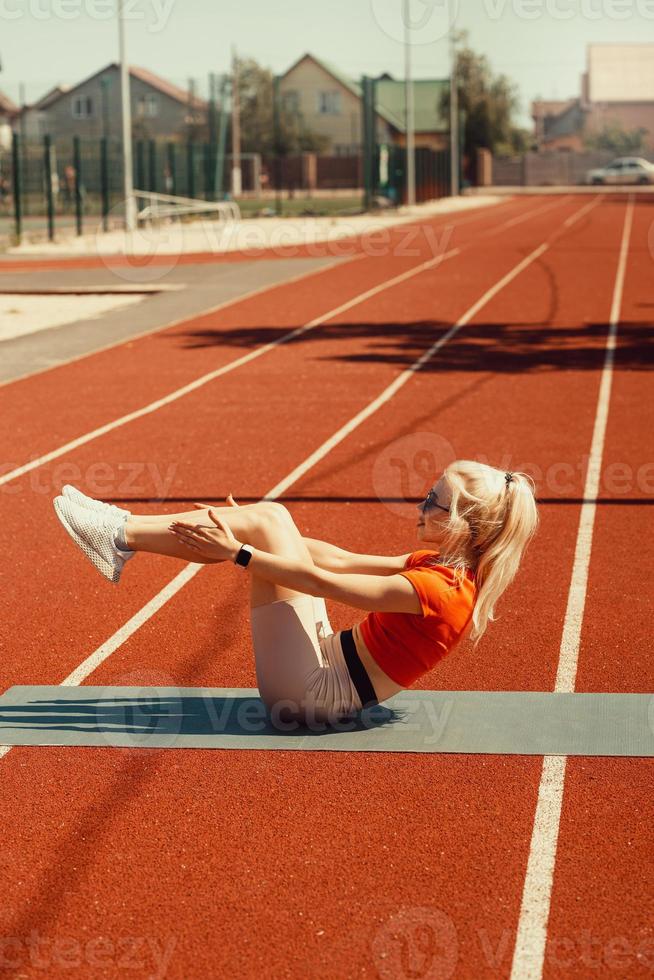 la giovane bionda scuote i muscoli addominali su un tappetino sportivo per strada foto