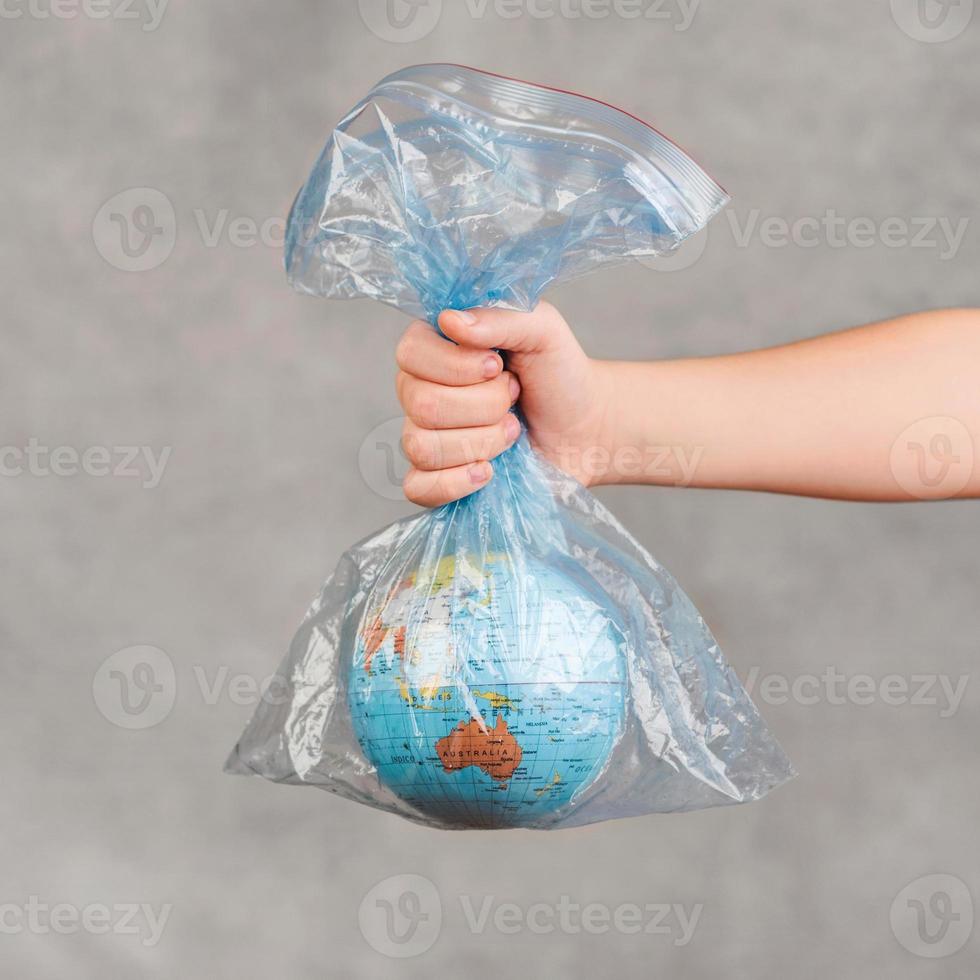 mano del bambino che tiene il globo terrestre in un sacchetto di plastica trasparente foto