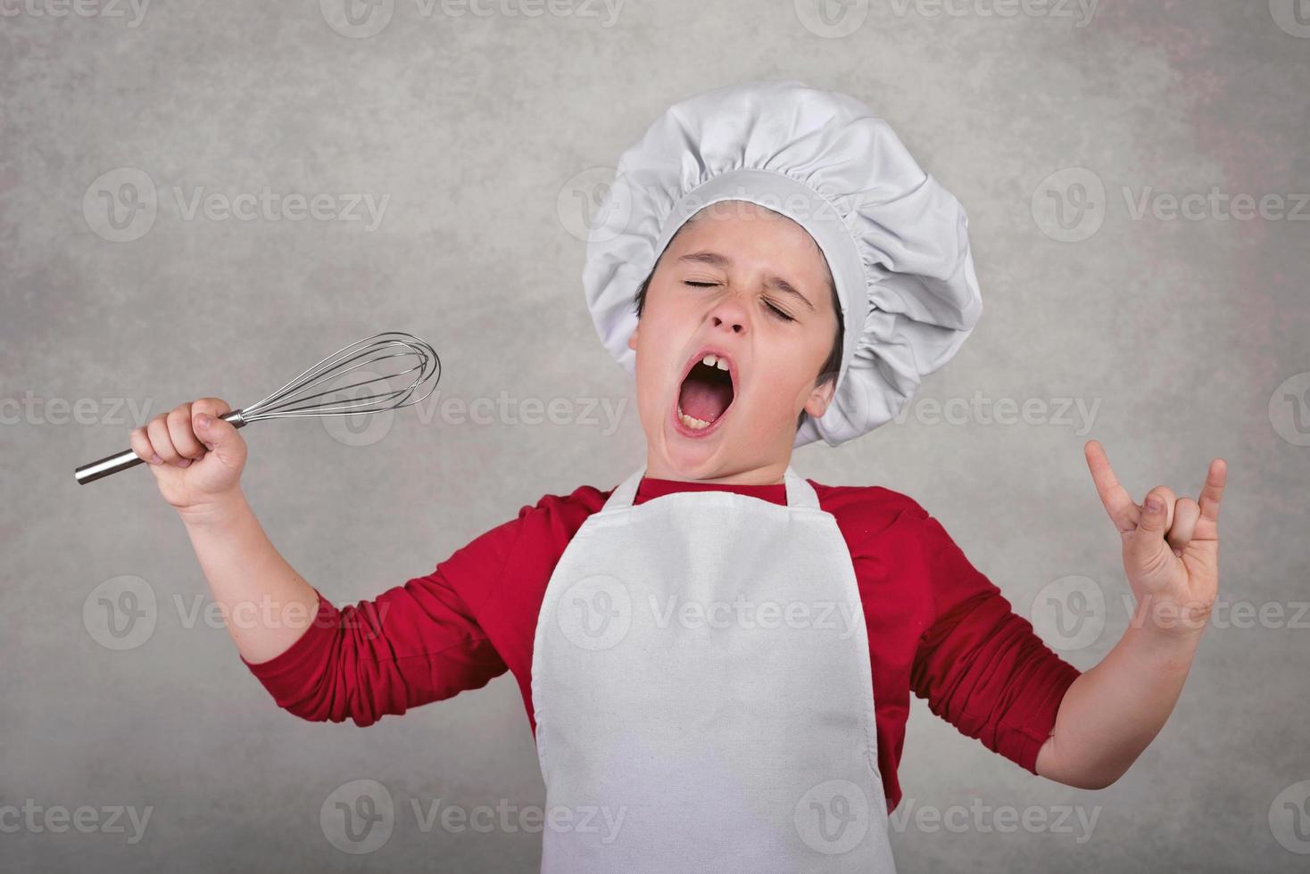 ragazzo divertente con cappello da cuoco che tiene la frusta in una mano foto