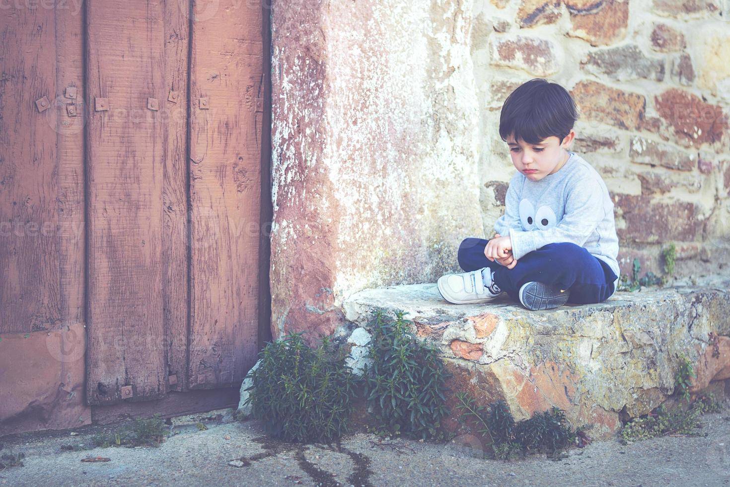 bambino triste seduto accanto a una porta foto