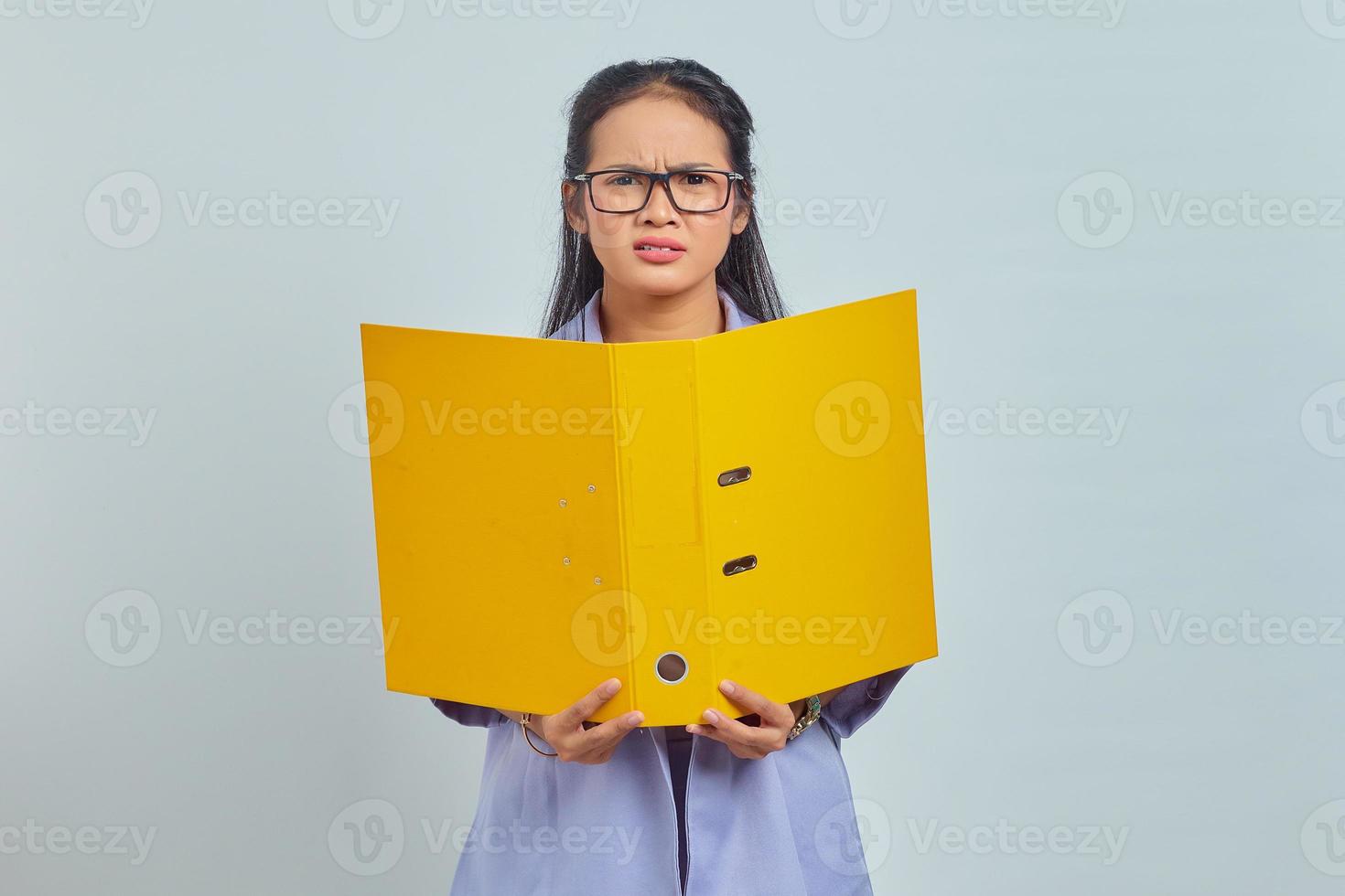 ritratto di giovane donna d'affari asiatica pensosa che tiene una cartella gialla isolata su sfondo viola foto