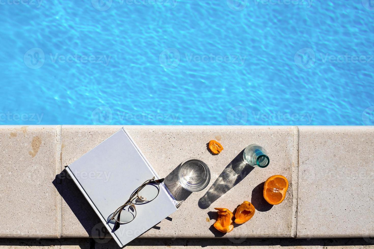 libro bianco con bicchieri e frutta accanto alla piscina foto