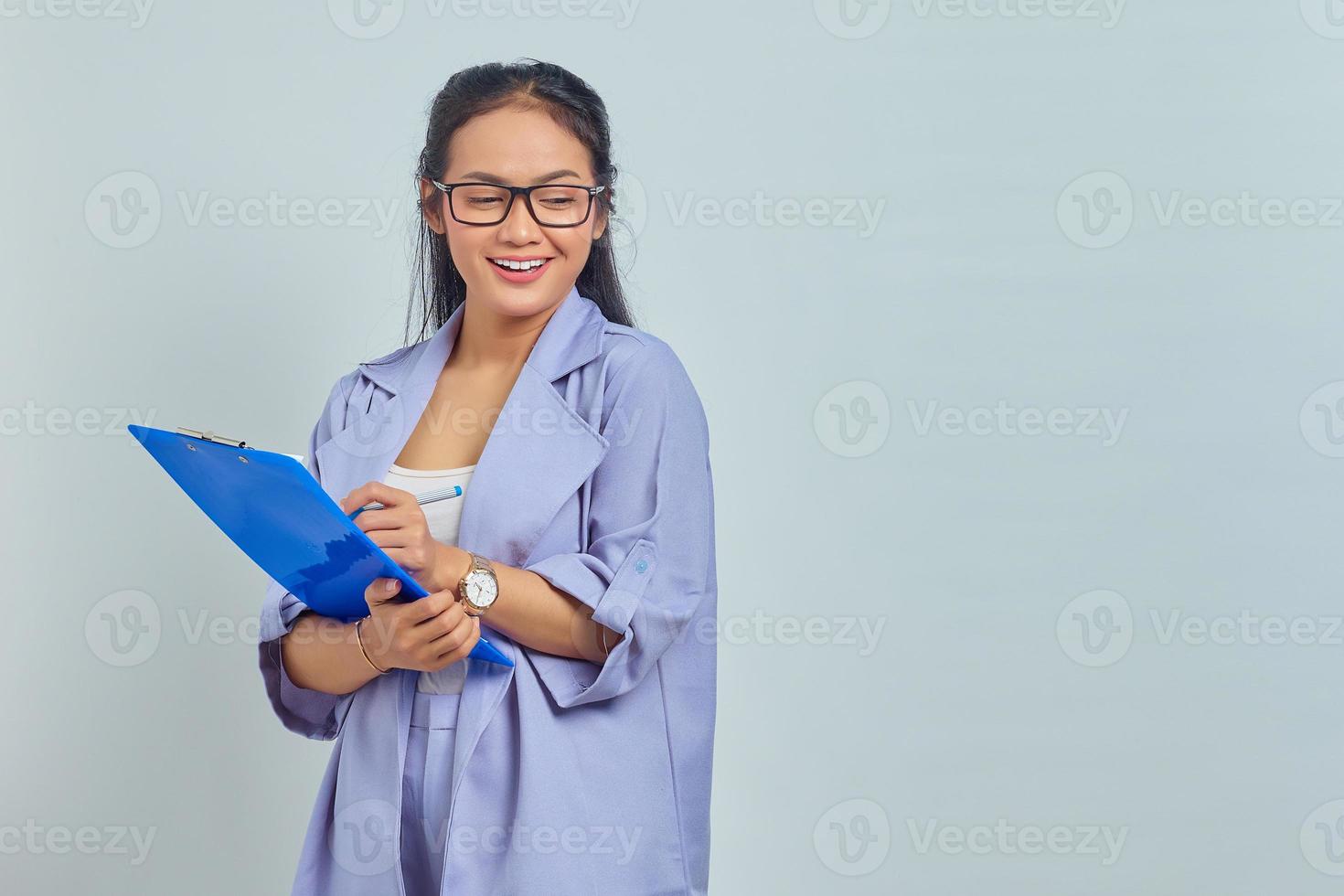 Ritratto di giovane e bella donna asiatica d'affari in tuta in piedi tenendo la cartella dei documenti con la faccia sorridente su sfondo viola foto