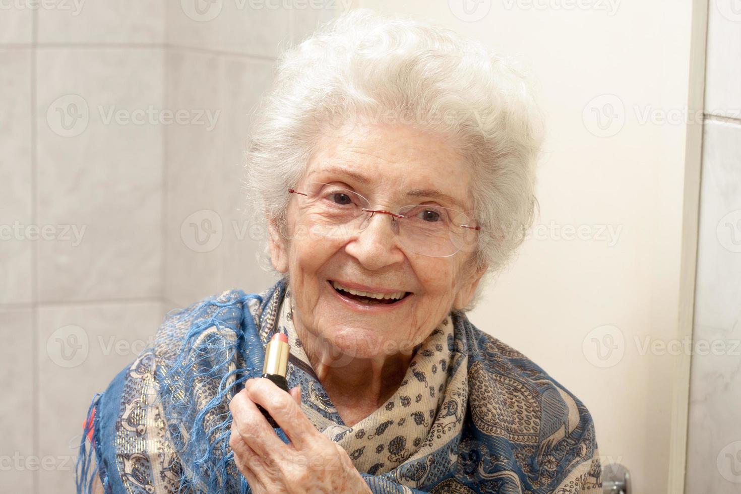 signora anziana che applica il rossetto davanti a uno specchio foto