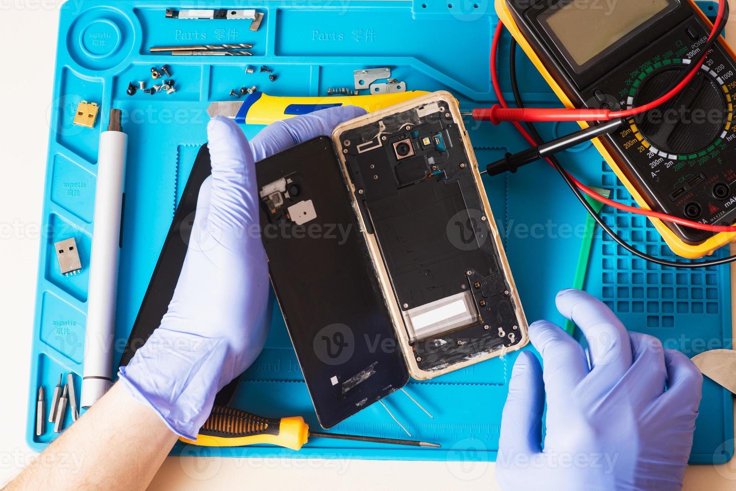 artigiano in guanti di gomma ripara o ripara un telefono cellulare su uno speciale tappetino in gomma per la riparazione. vista dall'interno foto