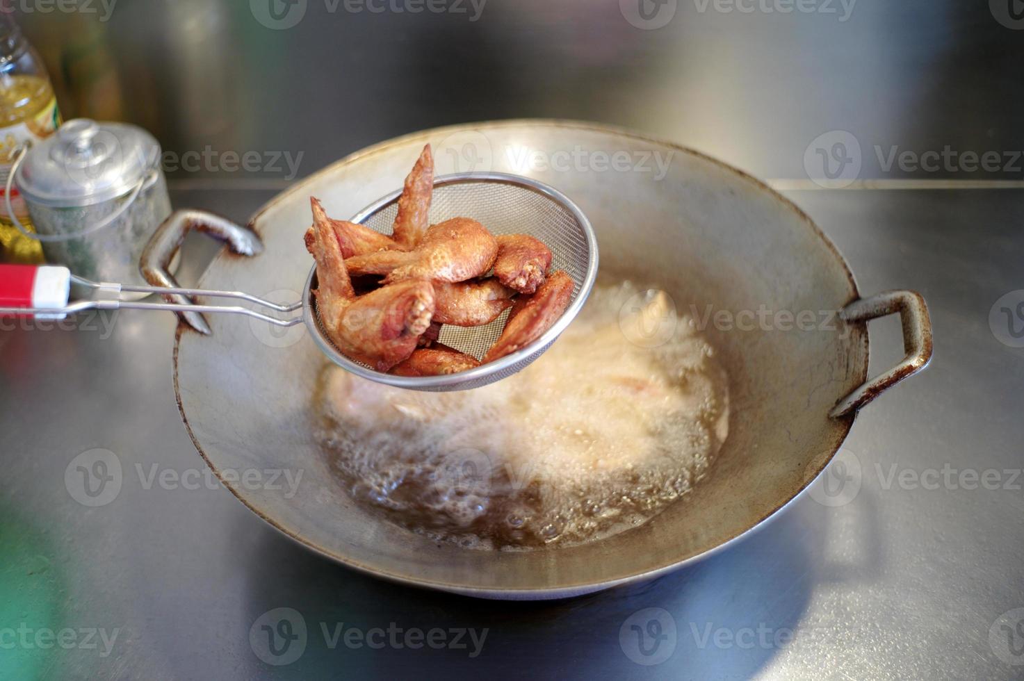 primo piano molti pezzi di ali di pollo fritte nel cestello inossidabile con verdure bollite sfocate foto