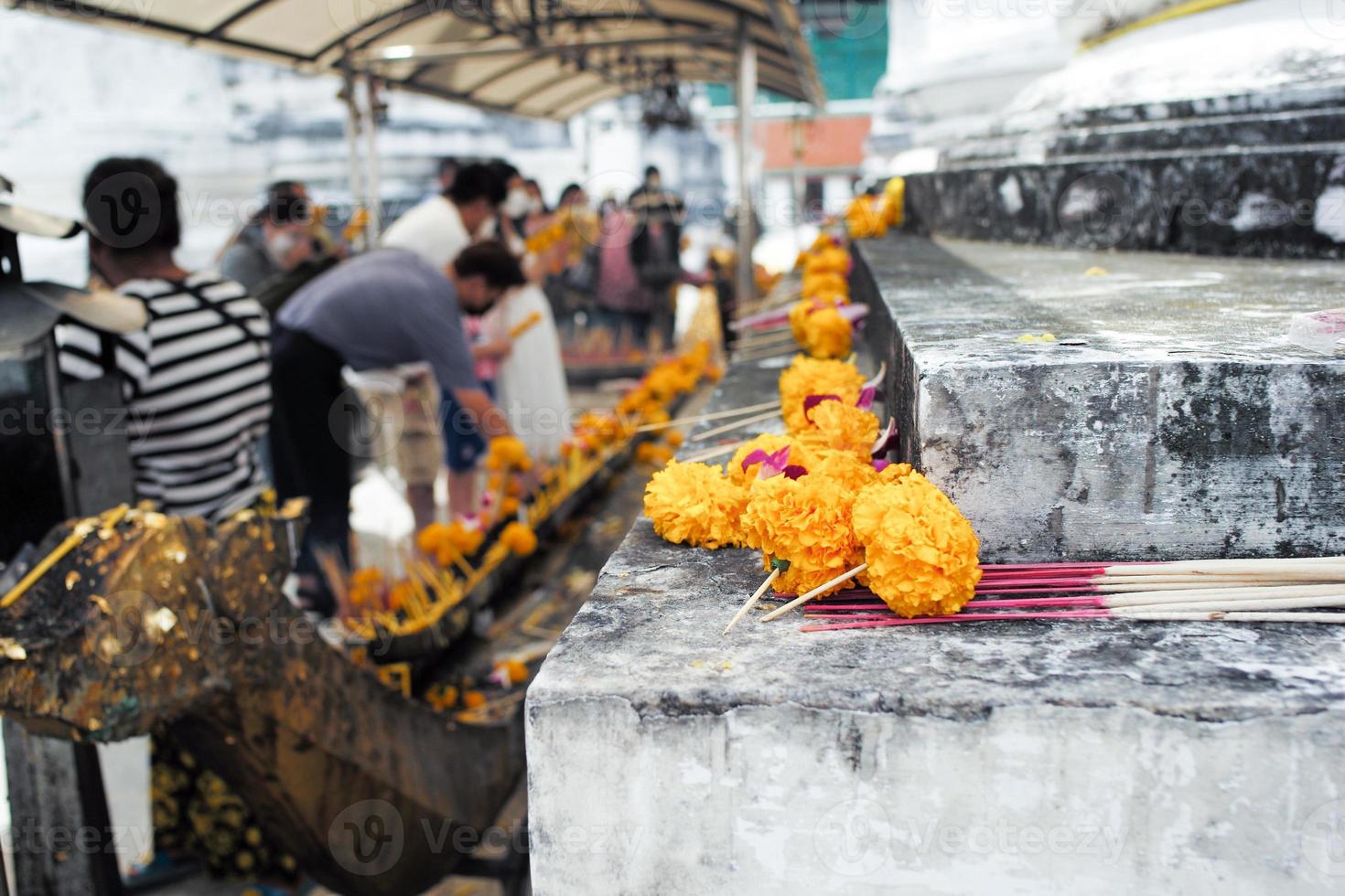 primo piano fiori di fiori di margherita messi sulla pagoda di cemento al tempio del buddismo con sfocato affollato di persone che pregano sullo sfondo foto