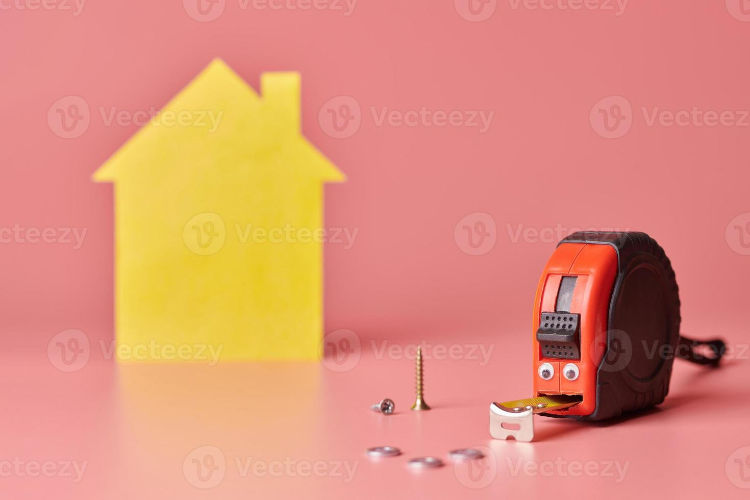 concetto divertente di misura di nastro di metallo. ristrutturazione casa. riparazione domestica e concetto ridecorato. figura a forma di casa gialla su sfondo rosa. foto