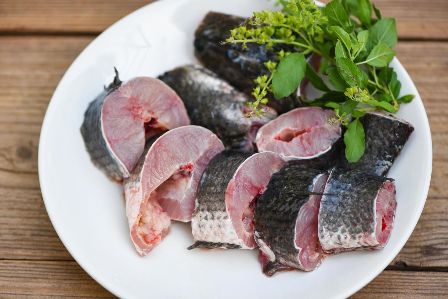 pesce testa di serpente per cucinare cibo, pesce testa di serpente a strisce tritato con ingredienti foglia di basilico santo su piatto bianco e tavolo in legno sfondo cucina, menu di pesce testa di serpente crudo fresco pesce d'acqua dolce foto