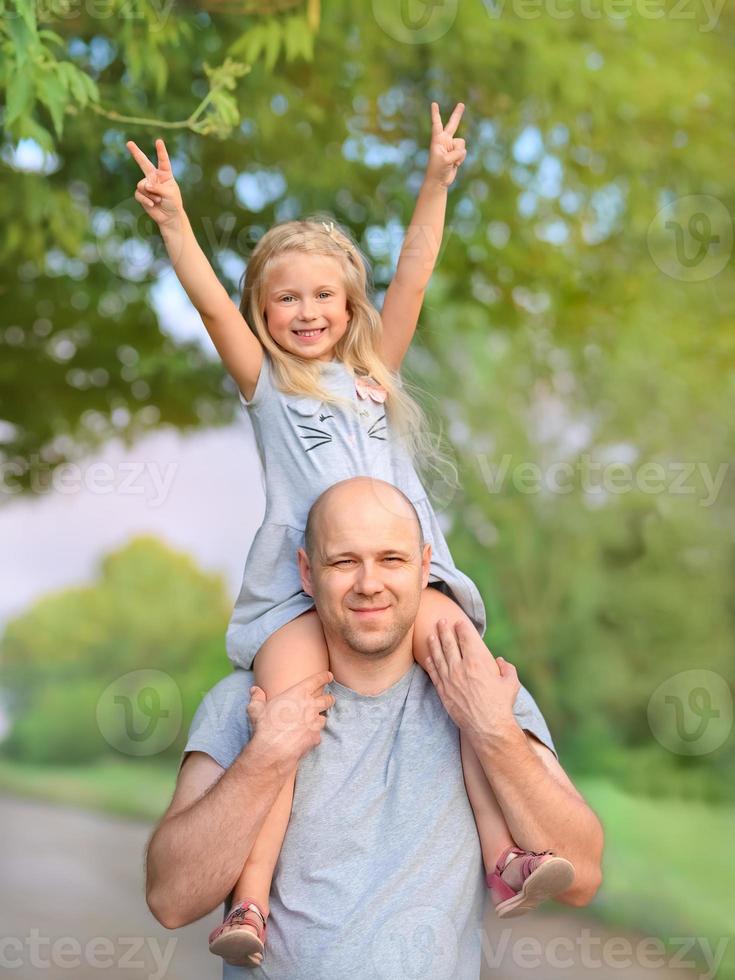 papà allegro che tiene la sua bambina felice sulle spalle, portandole le gambe foto