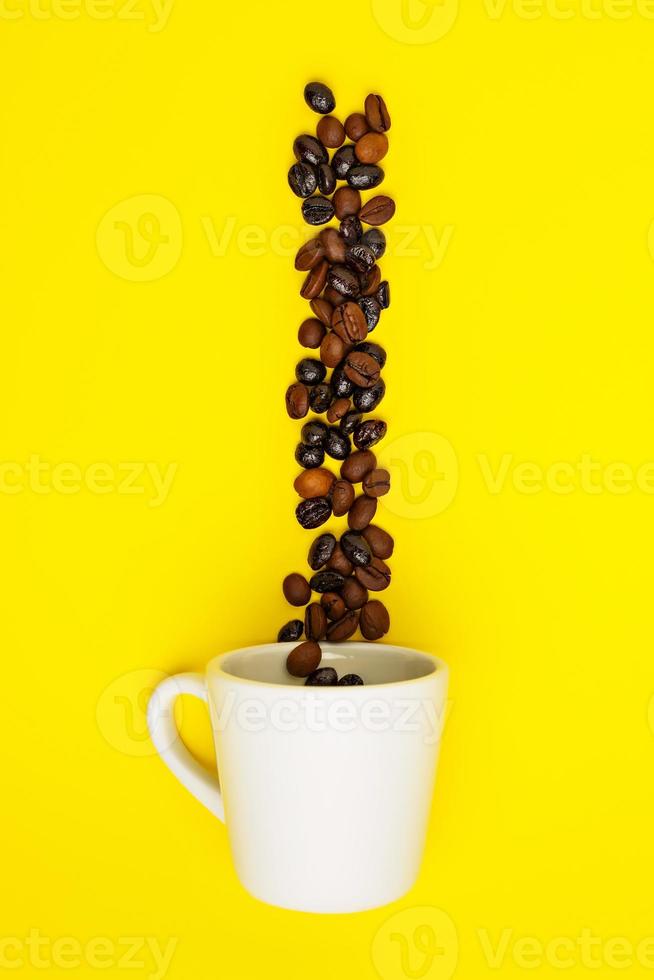 chicchi di caffè che cadono in una tazza bianca su sfondo giallo. foto