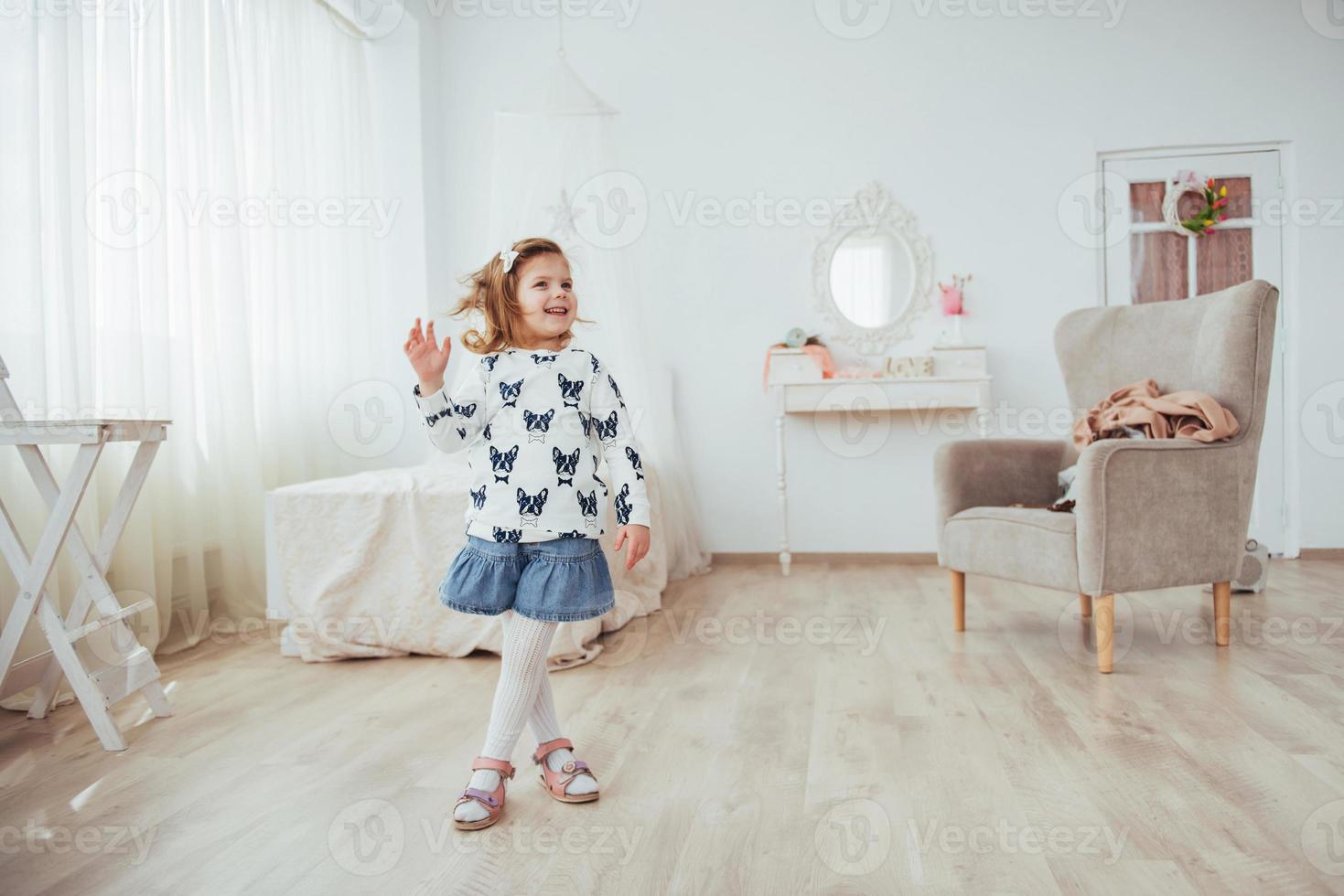 molto bella bionda affascinante bambina in piedi all'interno luminoso della casa, in piena vista foto