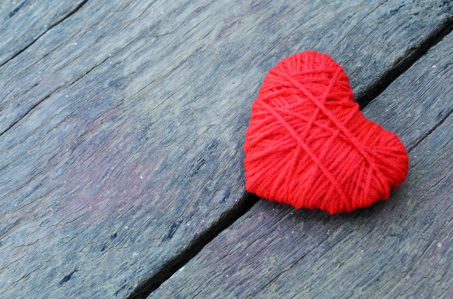 a forma di cuore rosso realizzato con filato di filo su fondo di legno vecchio per il concetto di San Valentino foto