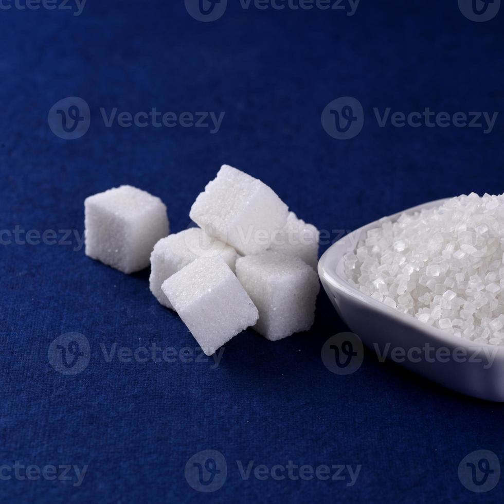 zollette di zucchero con zucchero in piatto bianco su sfondo blu foto
