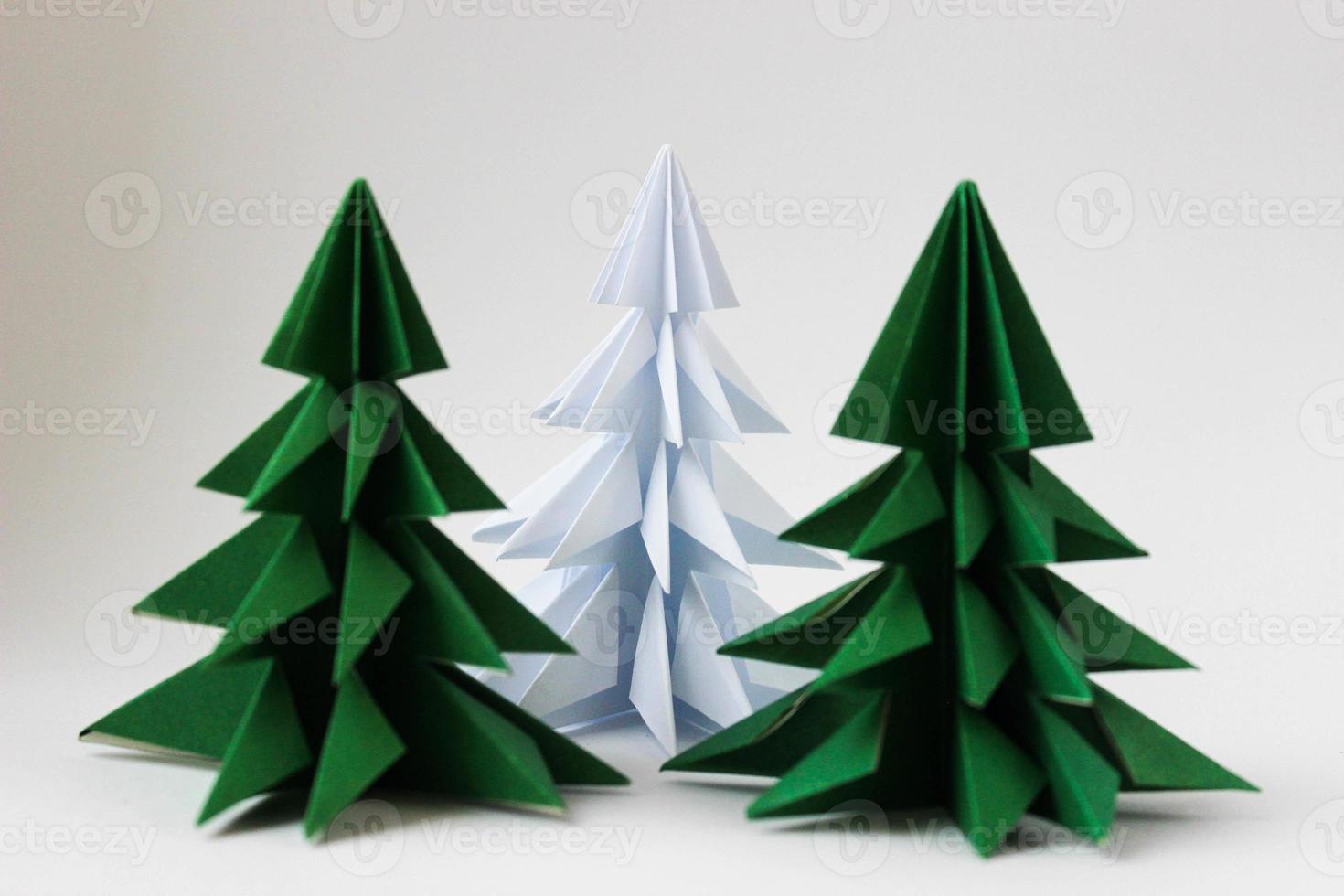 due alberi di natale verdi di origami e uno bianco su fondo bianco. foto