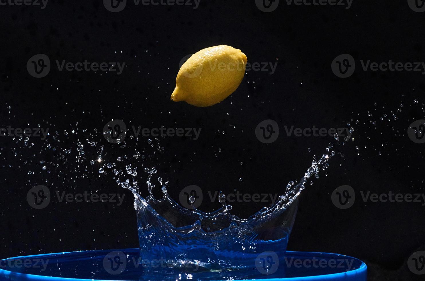 succoso limone giallo cade in acqua su sfondo nero foto