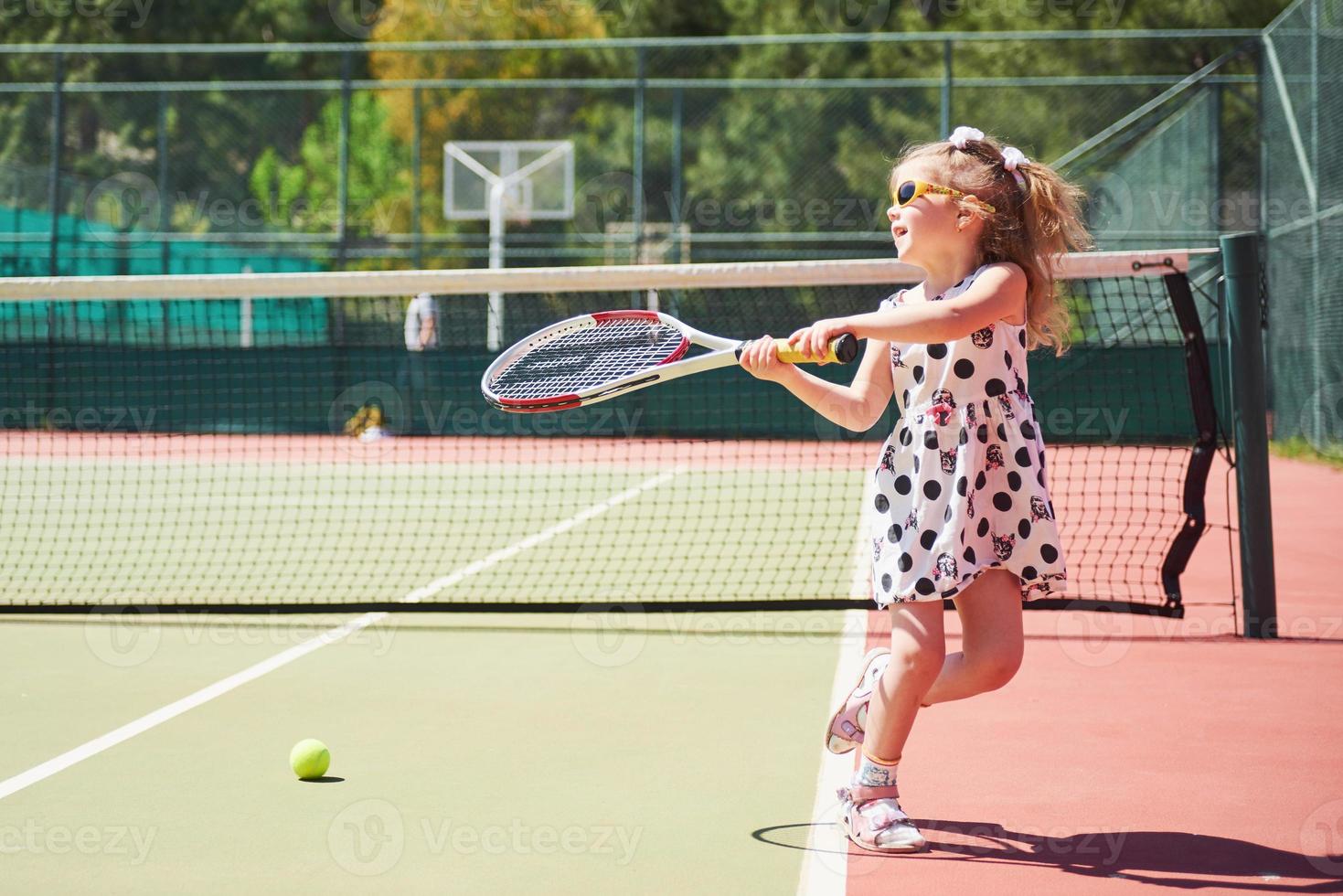 bambina sveglia che gioca a tennis sul campo da tennis all'esterno foto