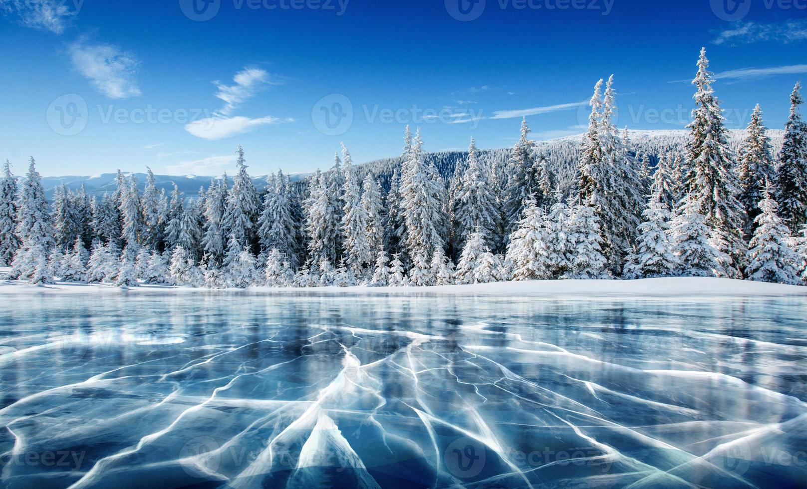 ghiaccio blu e crepe sulla superficie del ghiaccio. lago ghiacciato sotto un cielo blu in inverno. le colline dei pini. inverno. carpazi, ucraina, europa. foto