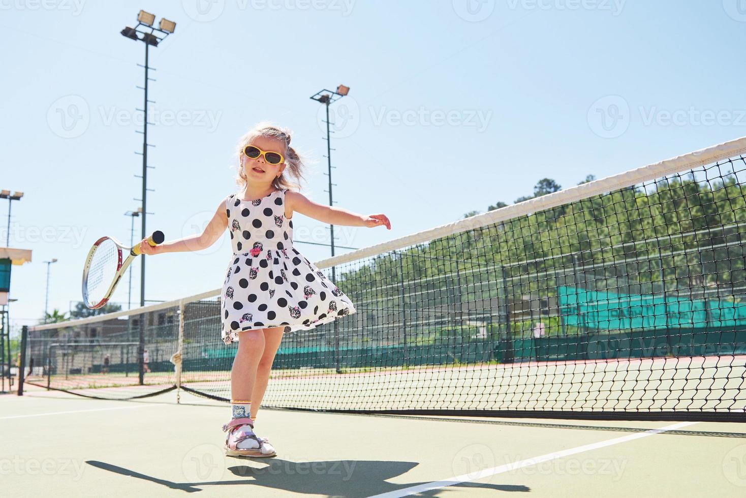 bambina sveglia che gioca a tennis sul campo da tennis all'esterno foto