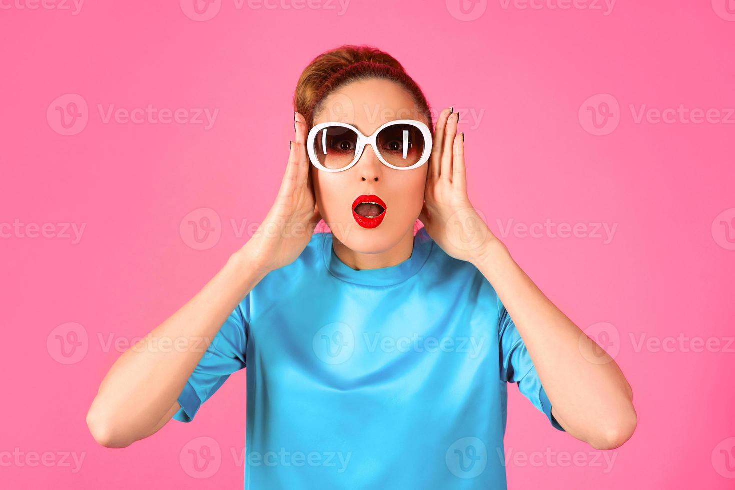 ritratto di giovane bella donna in abito di seta blu e occhiali da sole bianchi su sfondo rosa foto