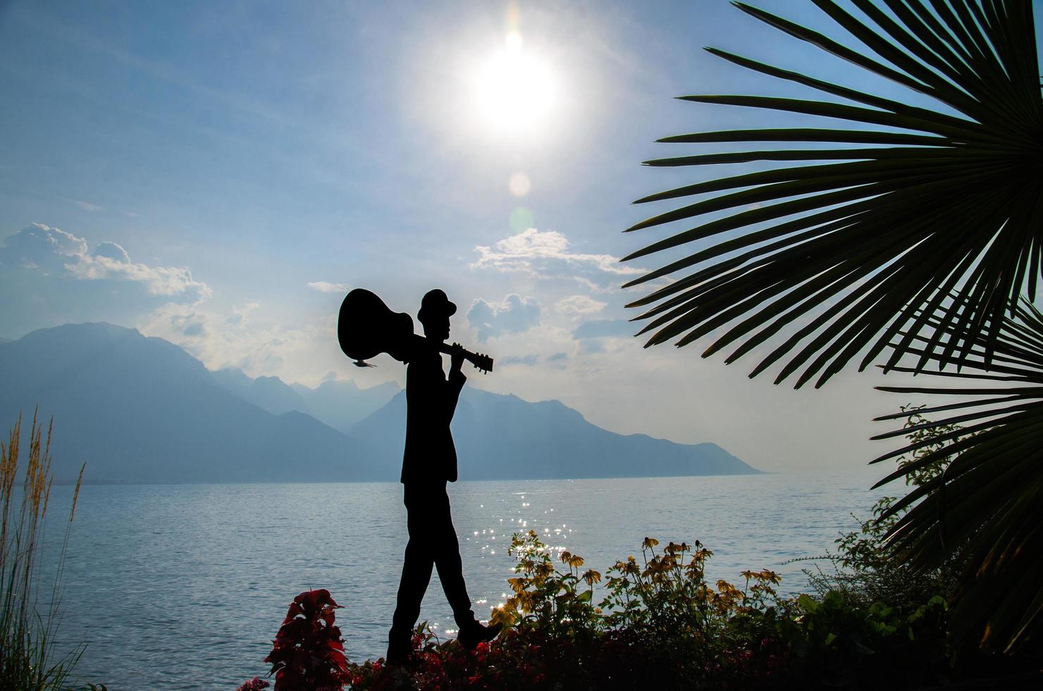 montreux, svizzera - 14 settembre 2017 figura silhouette di uomo con chitarra e fiori sulla passeggiata del lago lemano lago di ginevra davanti alle montagne alpi, riviera svizzera, cantone di vaud foto