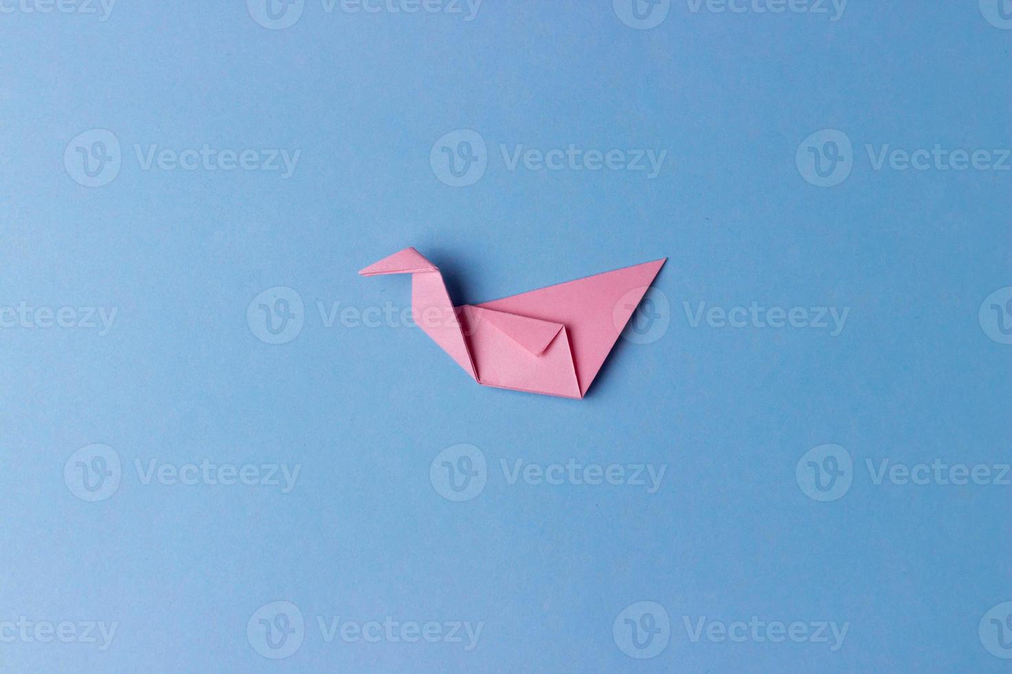 un uccello origami piegato da carta rosa su sfondo blu al centro della foto