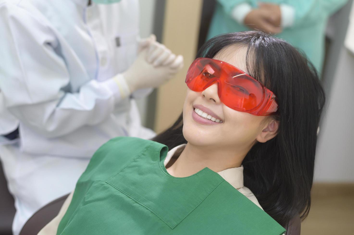 una donna che indossa occhiali protettivi che esamina da uno stomatologo, sbiancamento dei denti con lampada a raggi ultravioletti foto