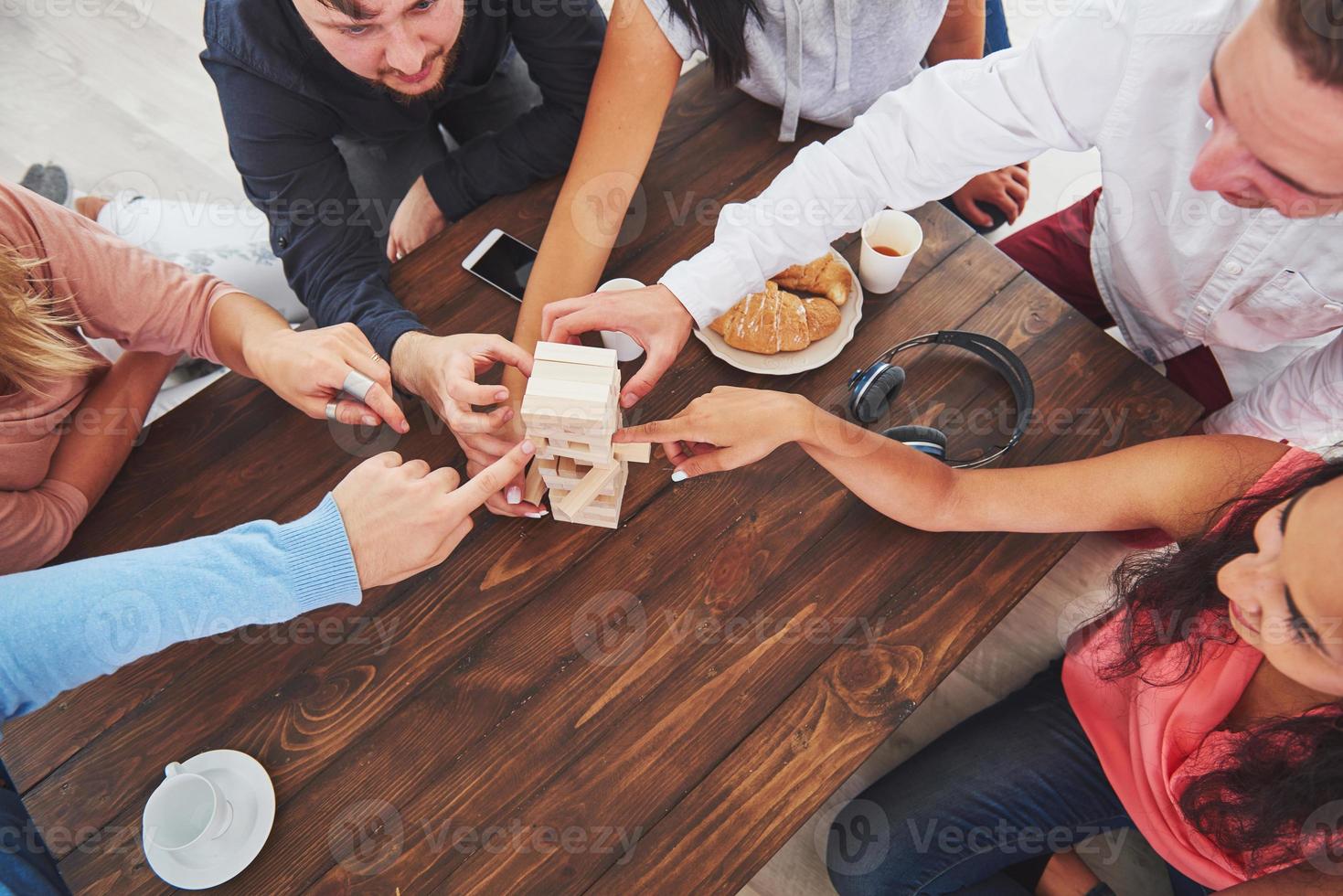 vista dall'alto foto creativa di amici seduti al tavolo di legno. amici che si divertono mentre giocano a un gioco da tavolo