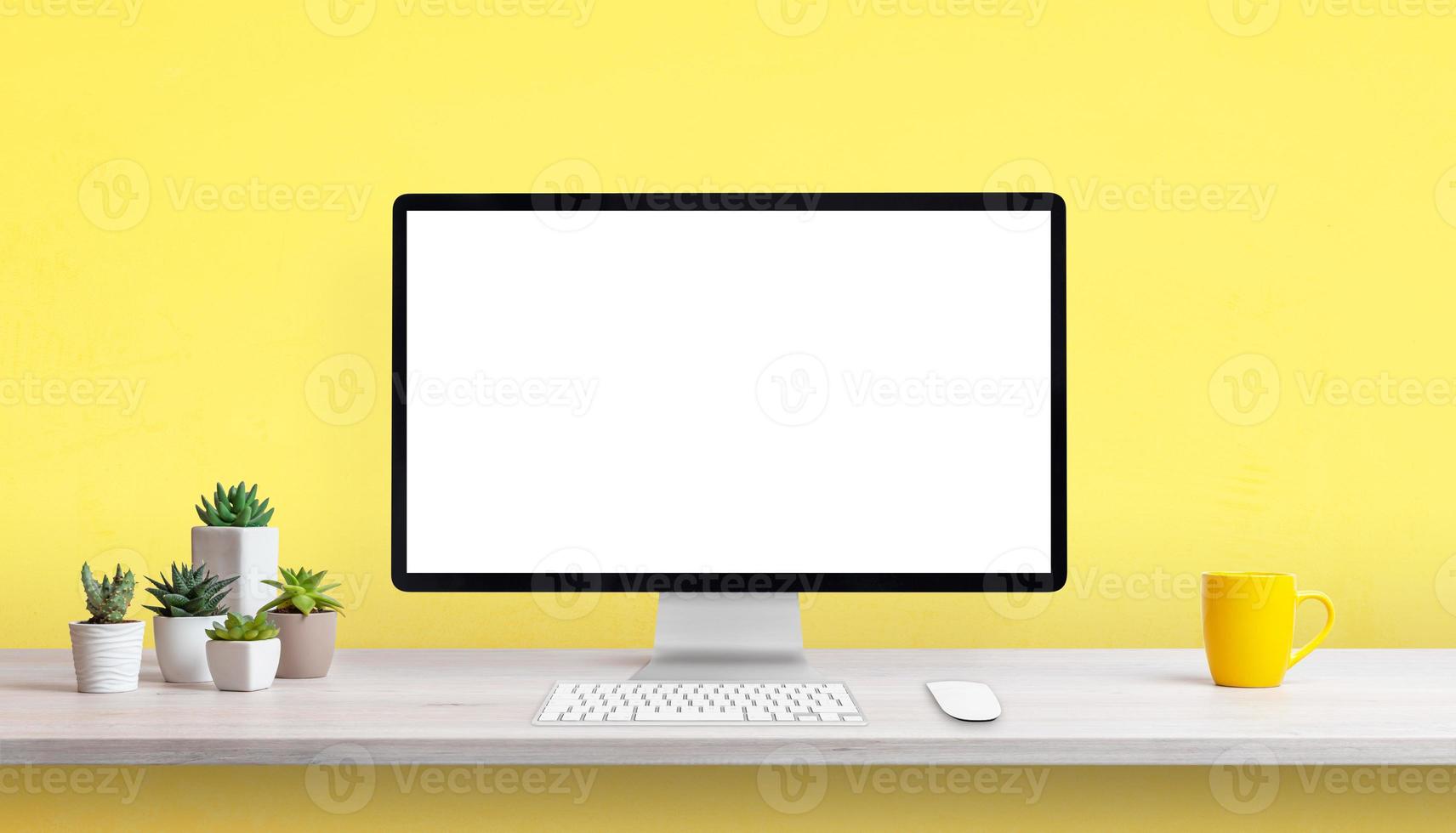 scrivania creativa con display per computer vuoto, tazza da caffè gialla e piante. sfondo giallo con spazio di copia foto