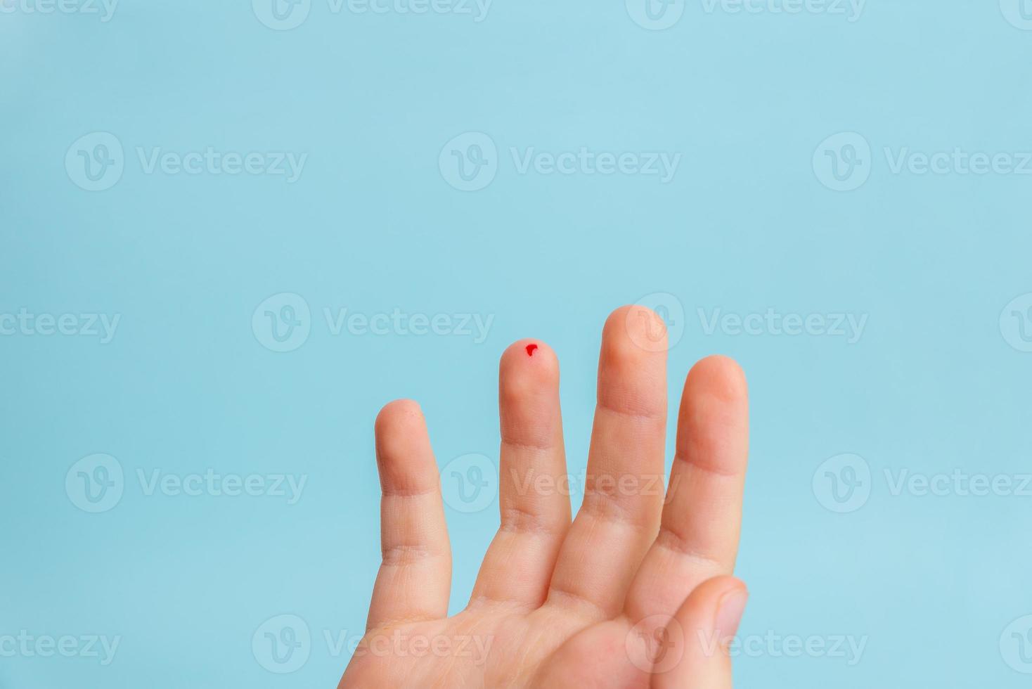 goccia di sangue sul dito di un bambino. il concetto di misurare i livelli di zucchero nel sangue con l'aiuto di strisce. sfondo blu foto