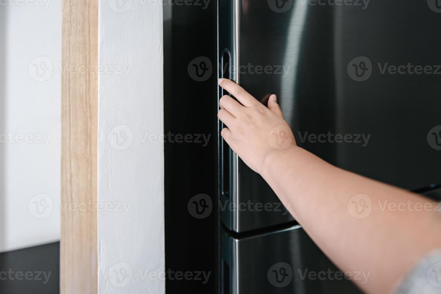 il primo piano della mano femminile è la porta del frigorifero aperta, frigorifero per alimenti freschi nella cucina. frigorifero per congelare alimenti per la salute foto