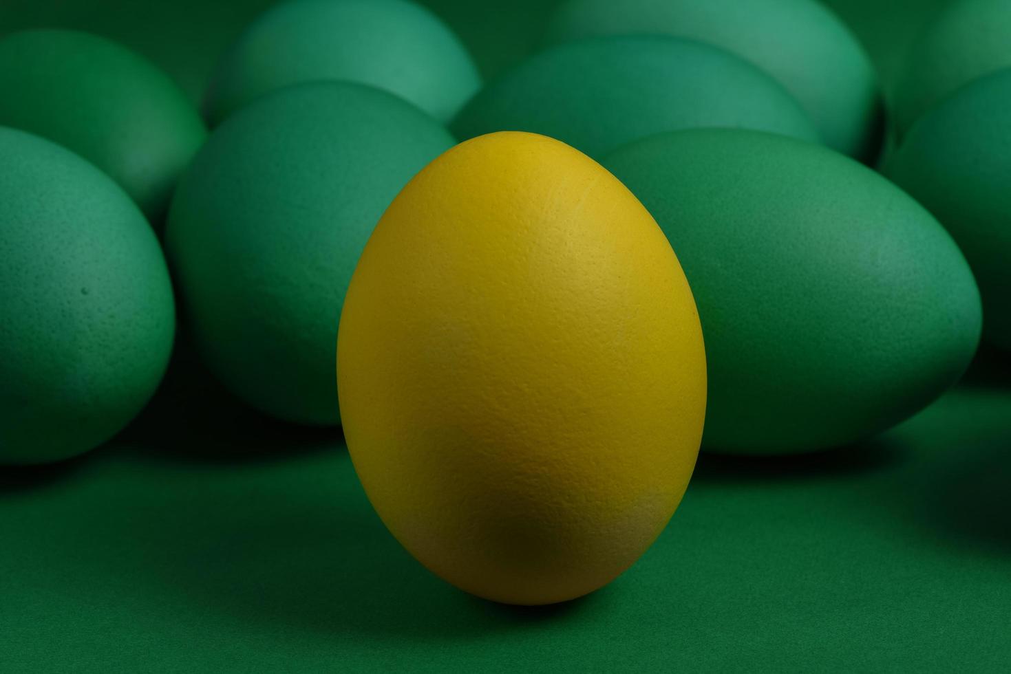 un uovo di Pasqua dipinto di giallo si trova di fronte a uova verdi su sfondo verde. foto