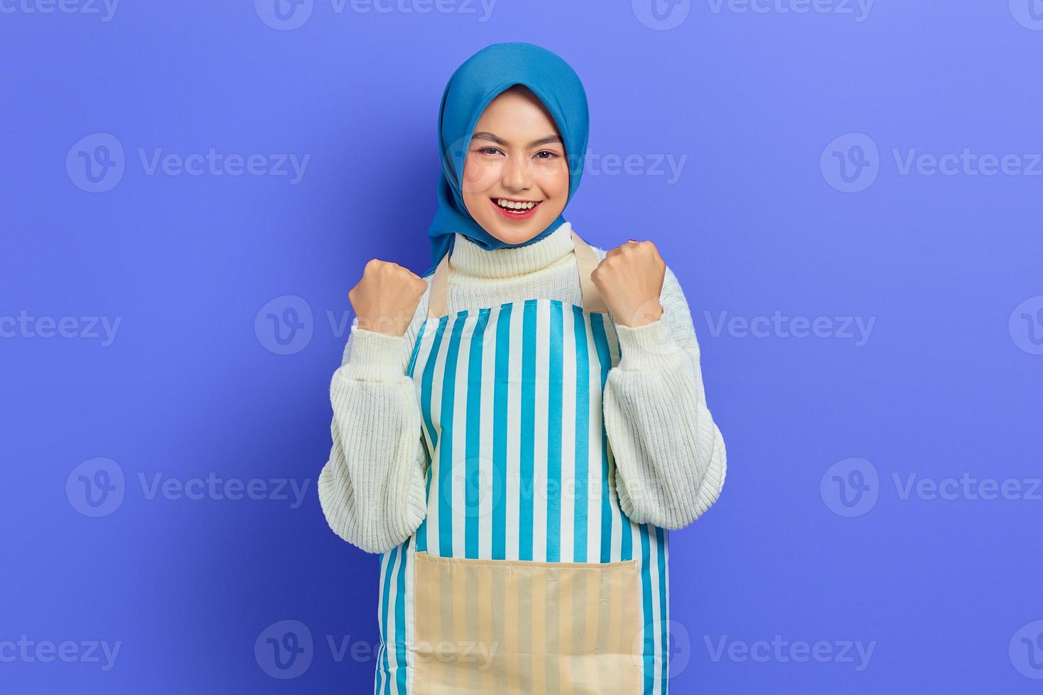 allegra giovane donna musulmana asiatica che indossa hijab e grembiule, celebrando il successo e ottenendo buone notizie isolate su sfondo viola. concetto di stile di vita musulmano casalinga di persone foto