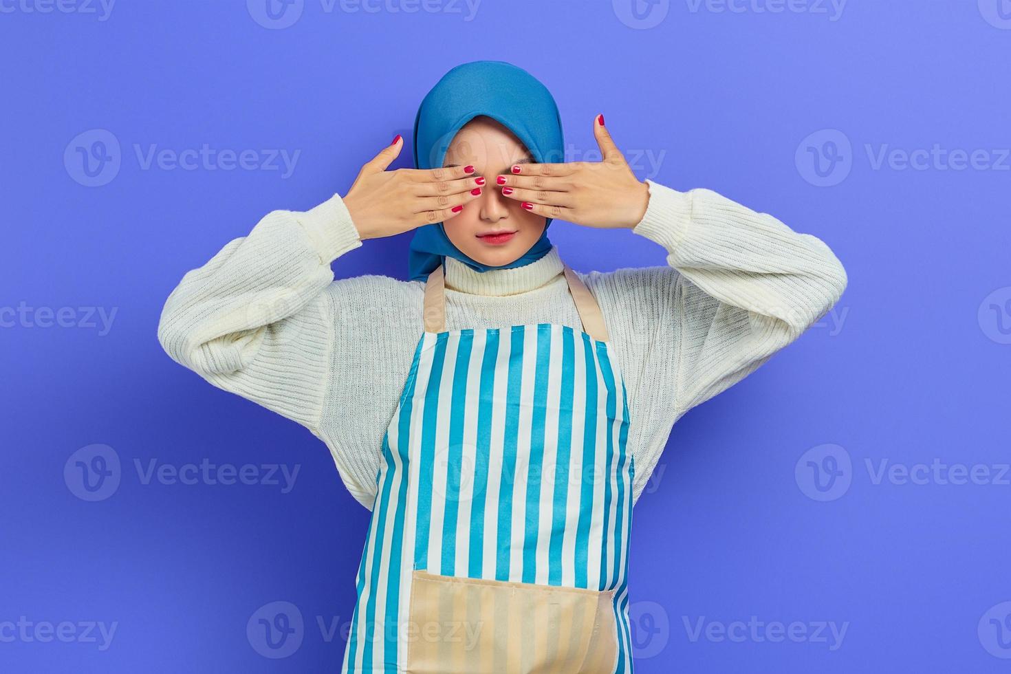 bella giovane donna casalinga in hijab e grembiule che copre gli occhi con le mani non vuole sembrare isolata su sfondo viola. concetto di stile di vita musulmano casalinga di persone foto