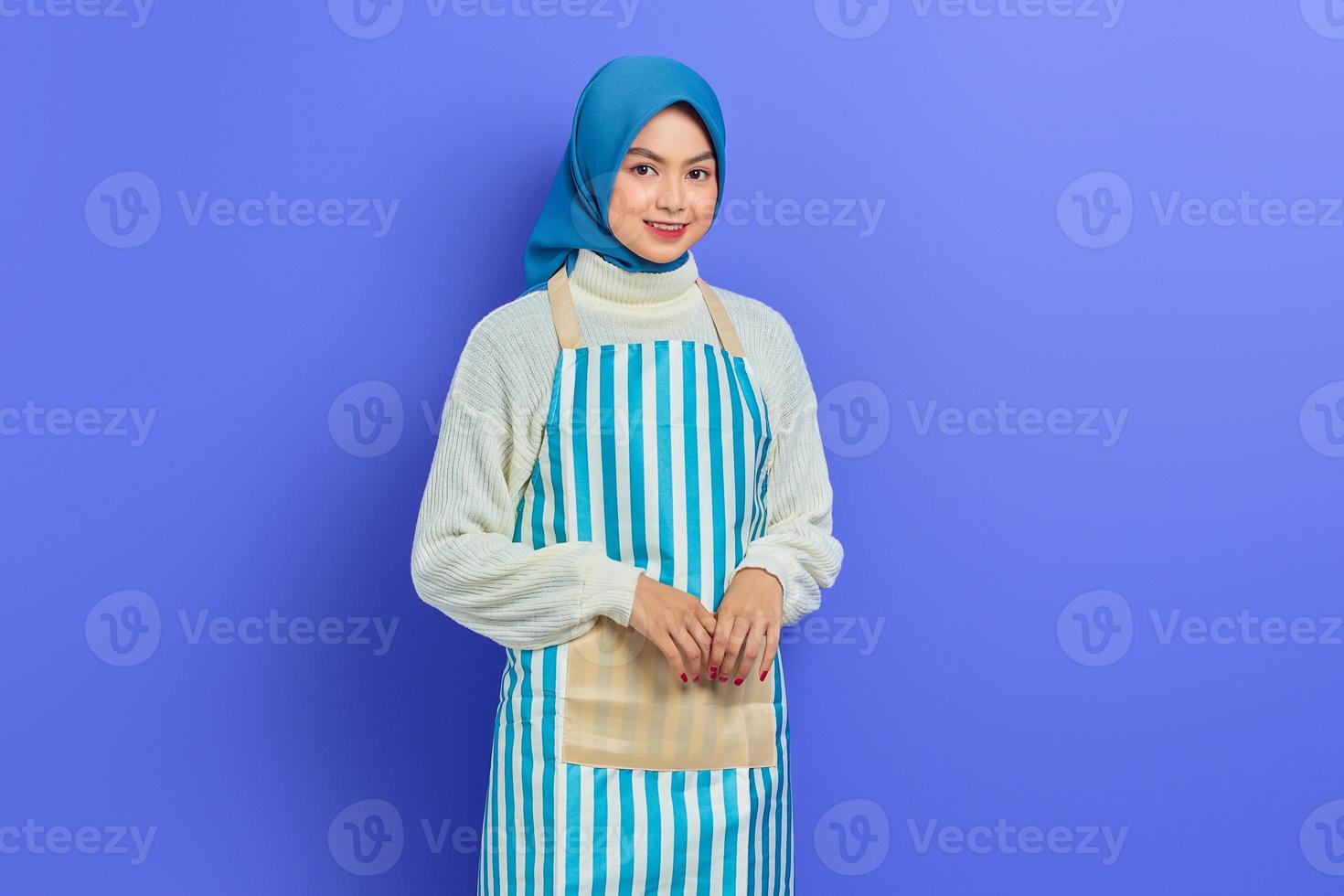 Ritratto di giovane donna musulmana asiatica sorridente che indossa hijab e grembiule, in piedi guardando la fotocamera isolata con sicurezza su sfondo viola. il concetto di uno stile di vita musulmano casalinga foto