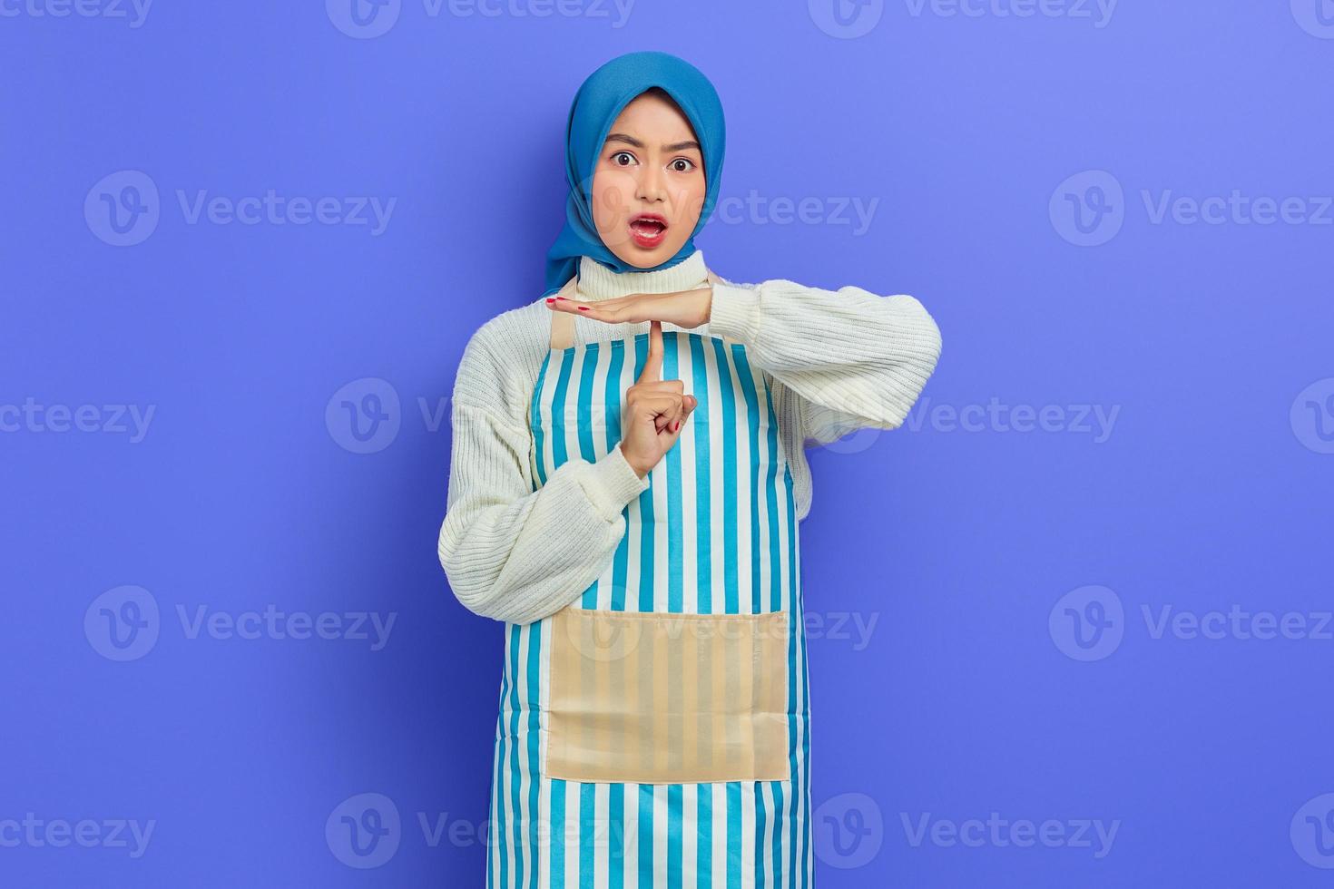 ritratto di una giovane casalinga scioccata in hijab e grembiule che mostra un gesto di timeout con le mani isolate su sfondo viola. concetto di stile di vita musulmano casalinga di persone foto
