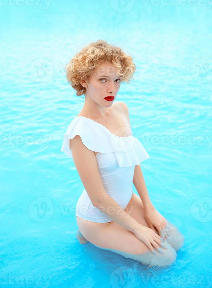 ritratto di donna rossa sorridente che si gode la vita in costume da bagno bianco in piscina foto