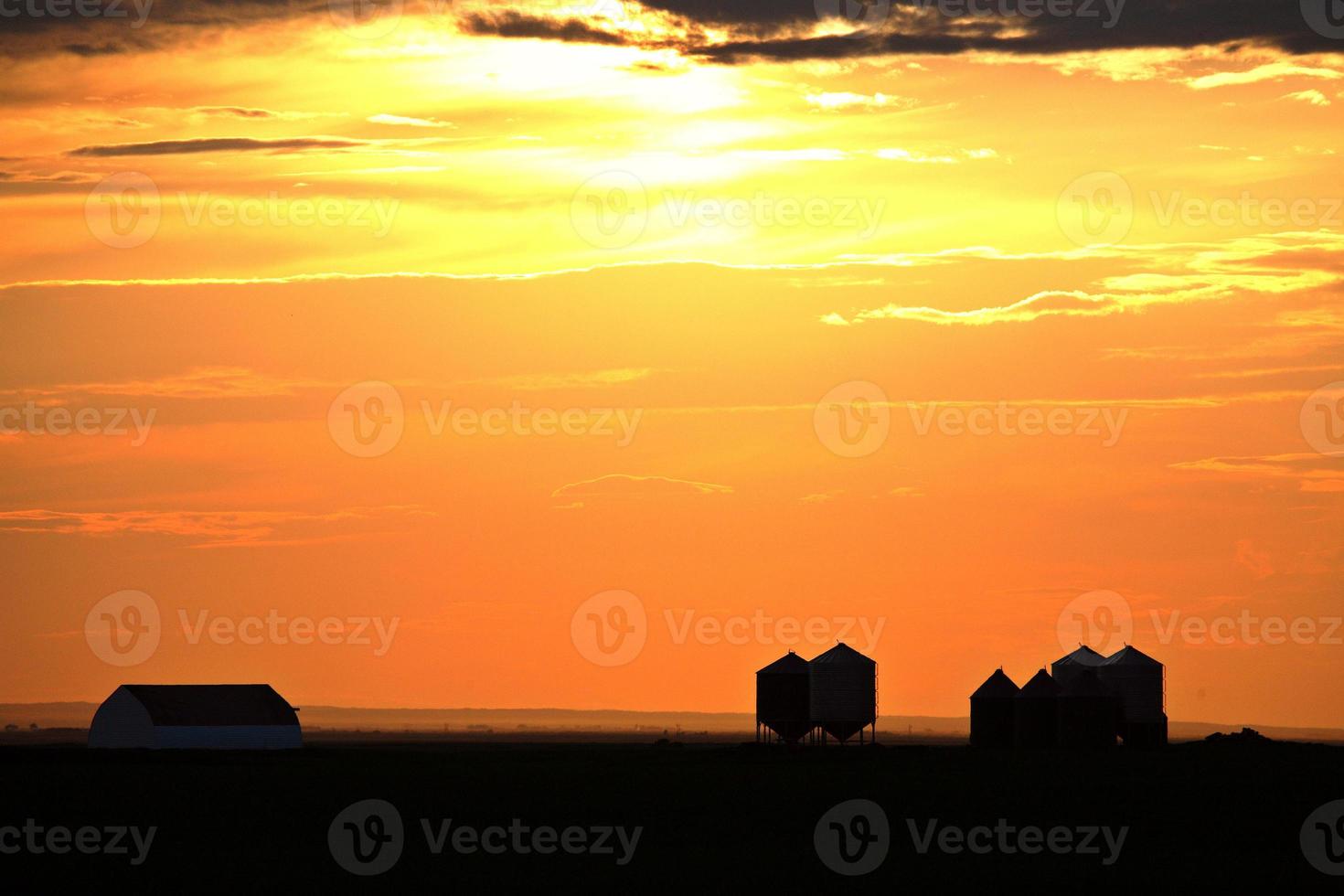 sole che tramonta illuminando gli edifici della fattoria nel pittoresco saskatchewan foto