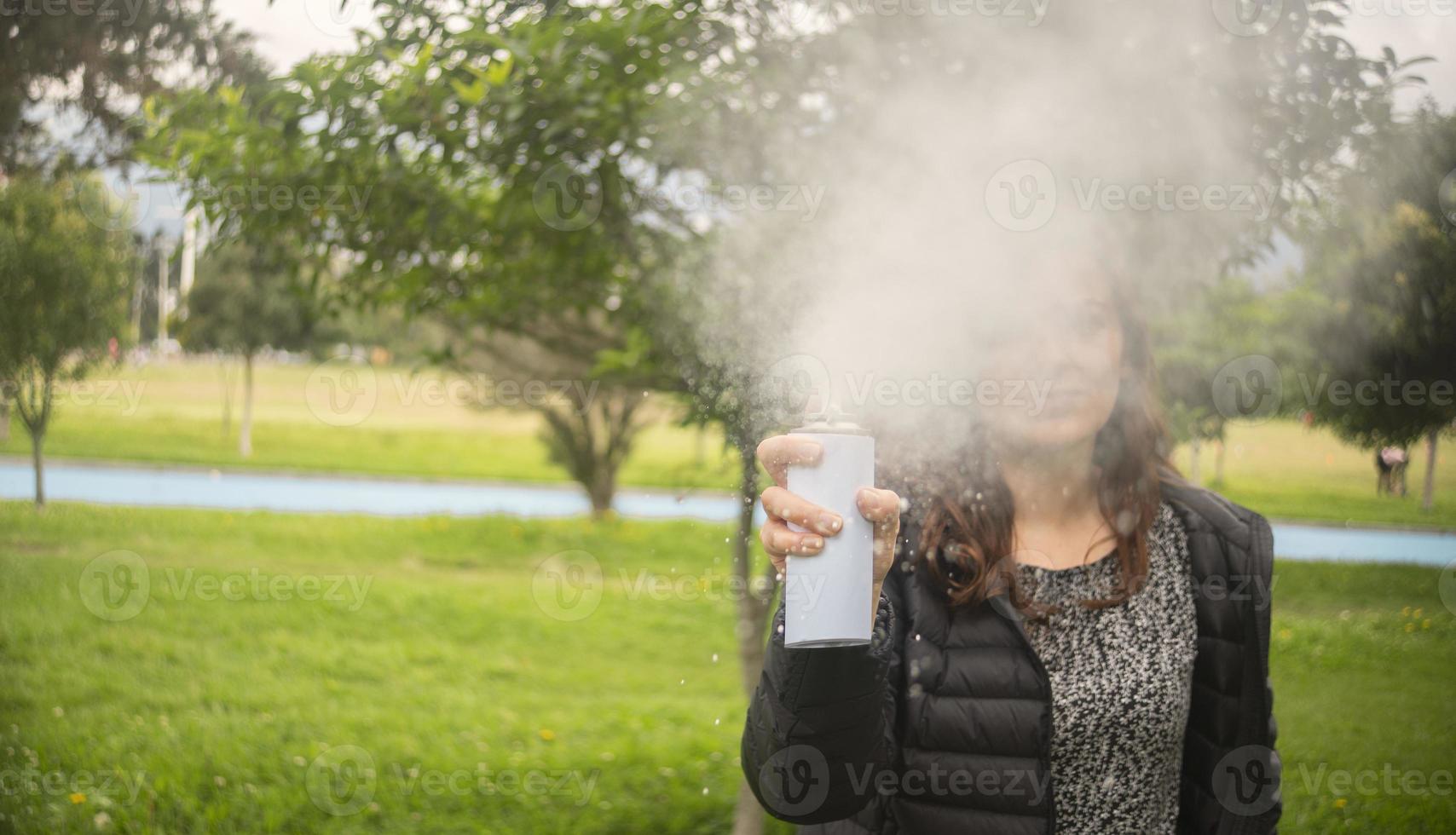 donna ispanica che spara un flusso di schiuma bianca da una bomboletta spray nel mezzo di un parco foto