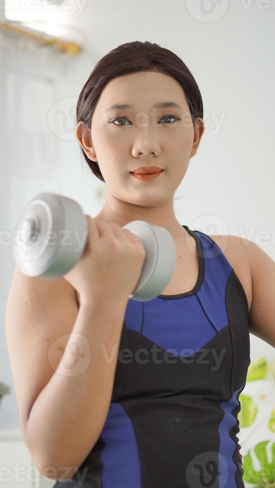 donna asiatica che solleva il bilanciere del braccio completo a casa foto
