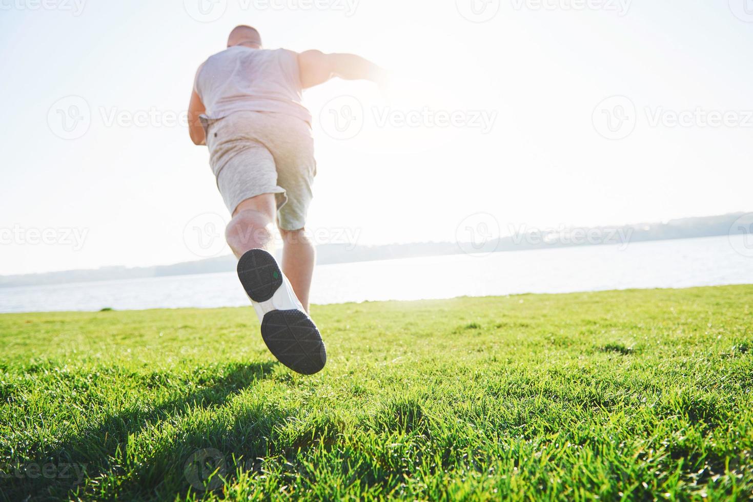 corsa campestre all'aperto nel sole estivo concetto per esercizio fisico, fitness e stile di vita sano. primo piano dei piedi di un uomo che corre nell'erba foto