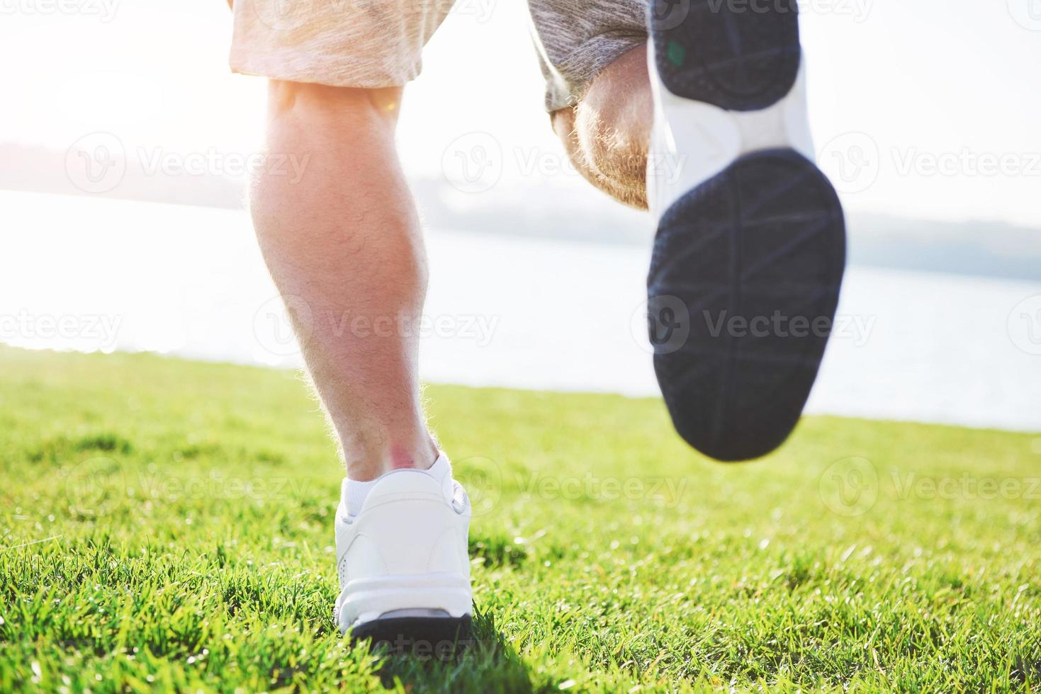 corsa campestre all'aperto nel sole estivo concetto per esercizio fisico, fitness e stile di vita sano. primo piano dei piedi di un uomo che corre nell'erba foto