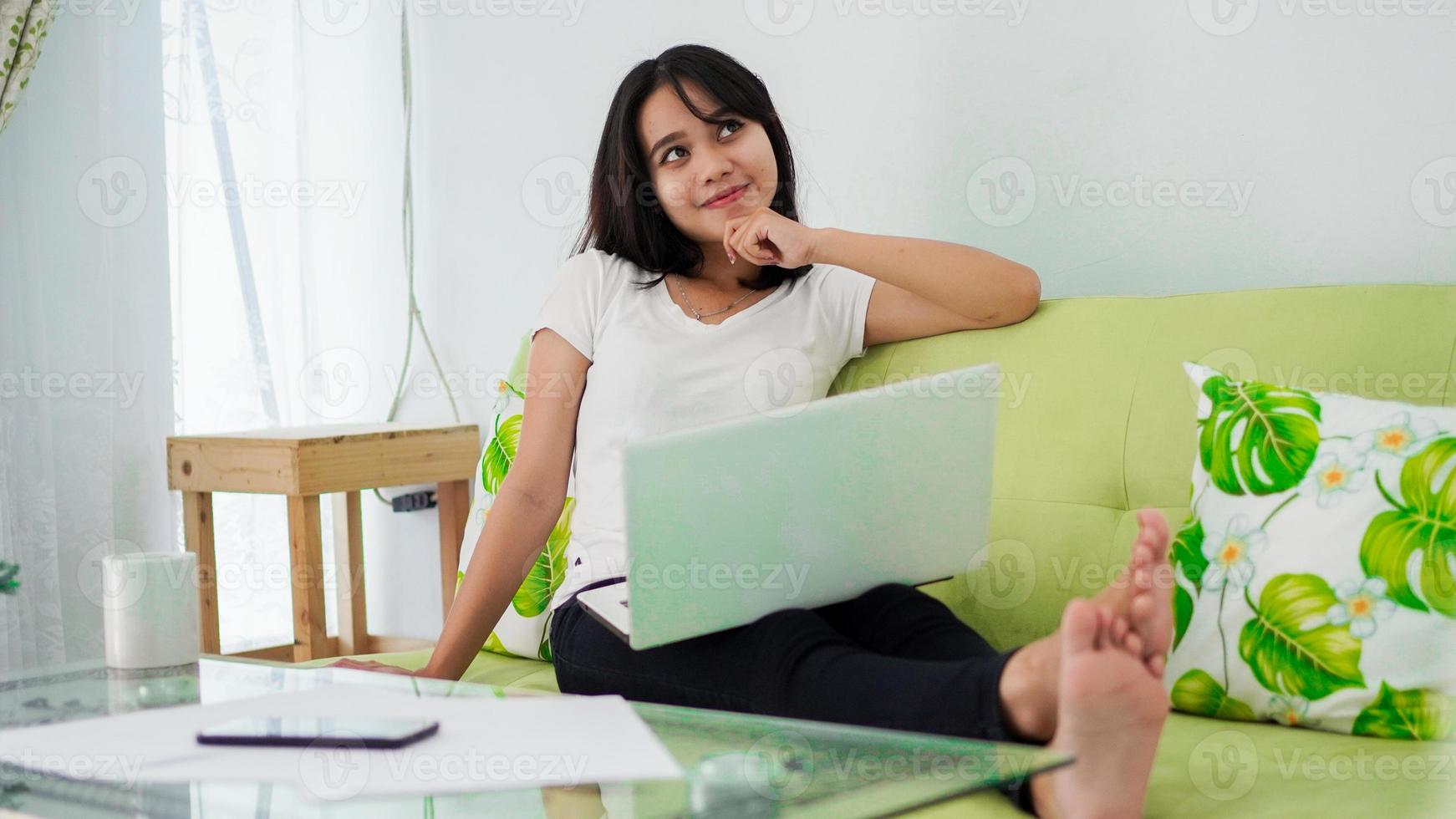 le donne asiatiche sedute su una sedia lavorano da casa al laptop e pensano alla soluzione del problema foto