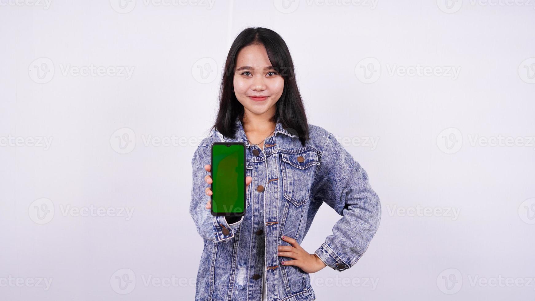 donne asiatiche sorridenti che indossano una giacca di jeans e tengono un telefono con schermo verde con sfondo bianco isolato foto