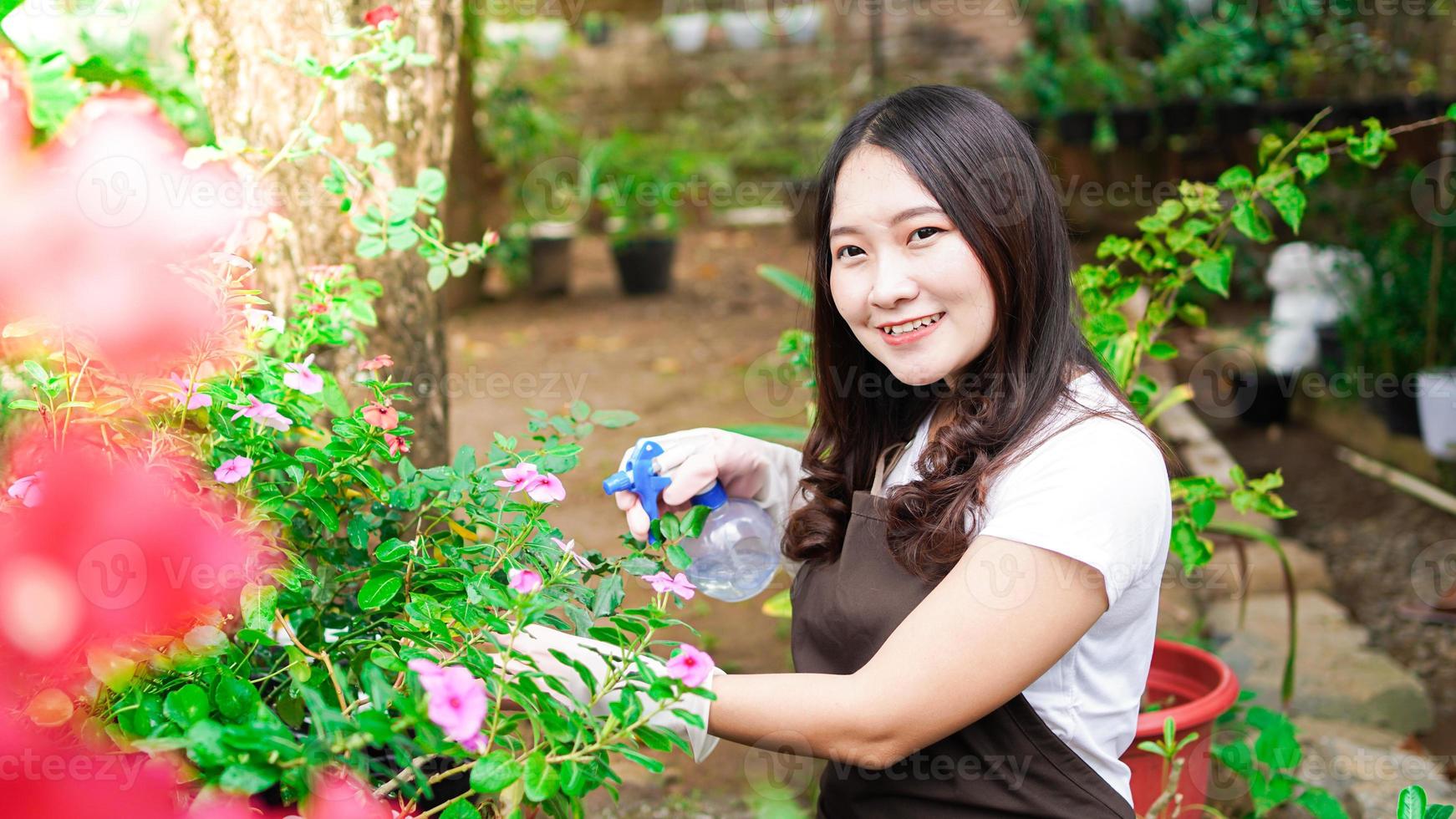 donna asiatica che si prende cura di annaffiare il fiore nel giardino di casa foto