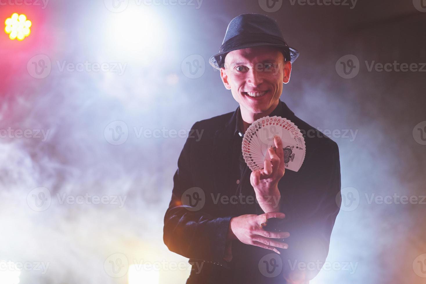 mago che mostra trucco con le carte da gioco. magia o destrezza, circo, gioco d'azzardo. prestigiatore in camera oscura con nebbia foto