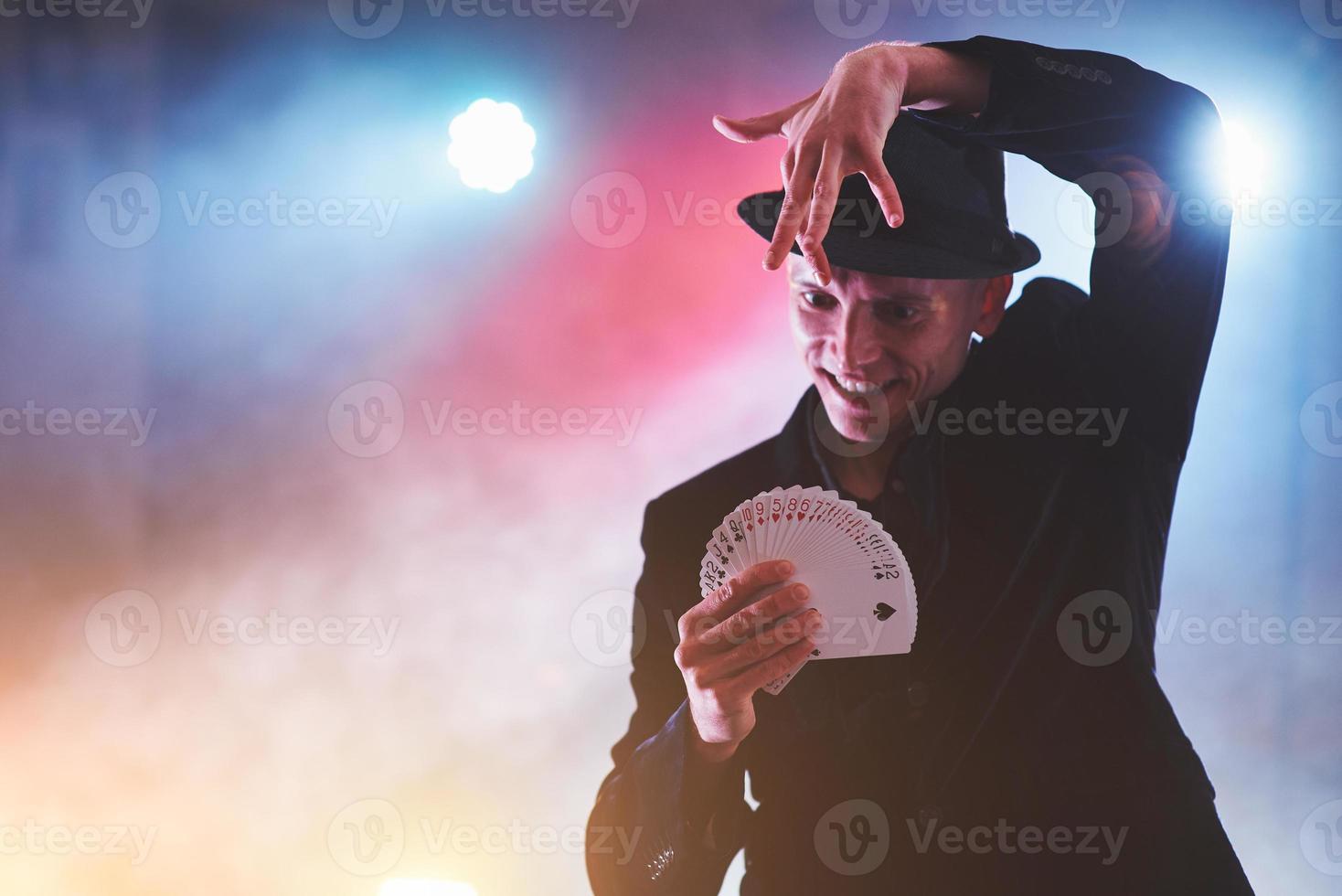 mago che mostra trucco con le carte da gioco. magia o destrezza, circo, gioco d'azzardo. prestigiatore in camera oscura con nebbia foto